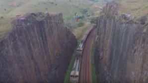 CASCADORIE ULUITOARE! Un bărbat a mers pe o sfoară întinsă între 2 stânci, în timp ce la sol se deplasa un tren (VIDEO)