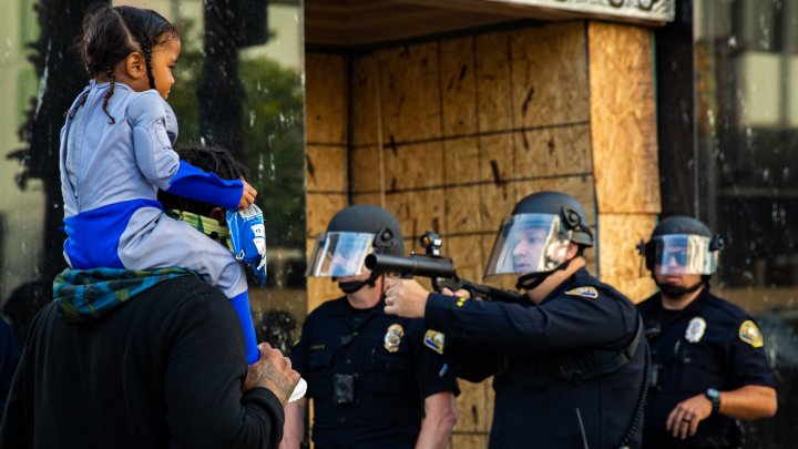 IMAGINE ŞOCANTĂ surprinsă în timpul protestelor din SUA. Polițist, cu arma scoasă și degetul pe trăgaci, în fața unei copile